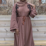 A woman wearing a brown open maysah abaya with floral embellishments on the shoulders