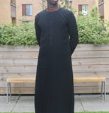 A man wearing a black emirati thobe
